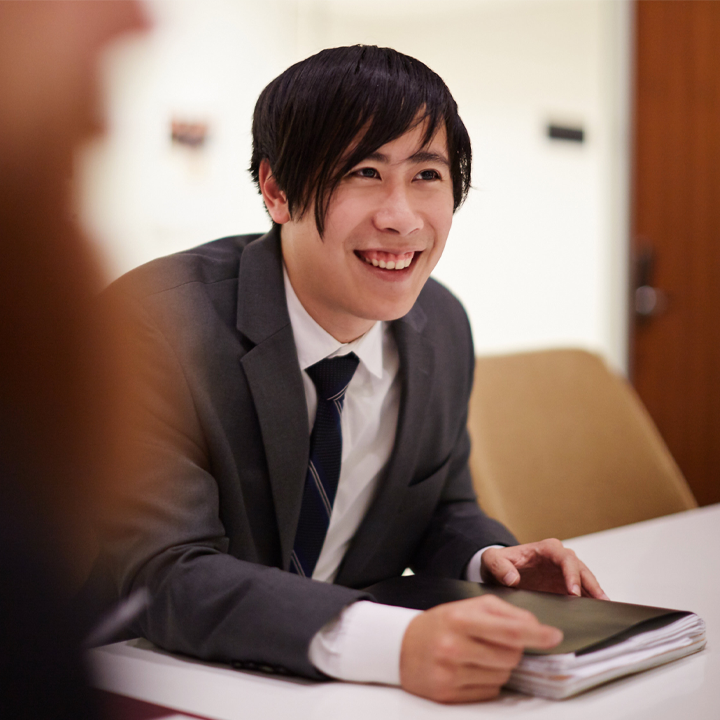A graduate student sitting at a table in a business suit with a notebook in front of them.